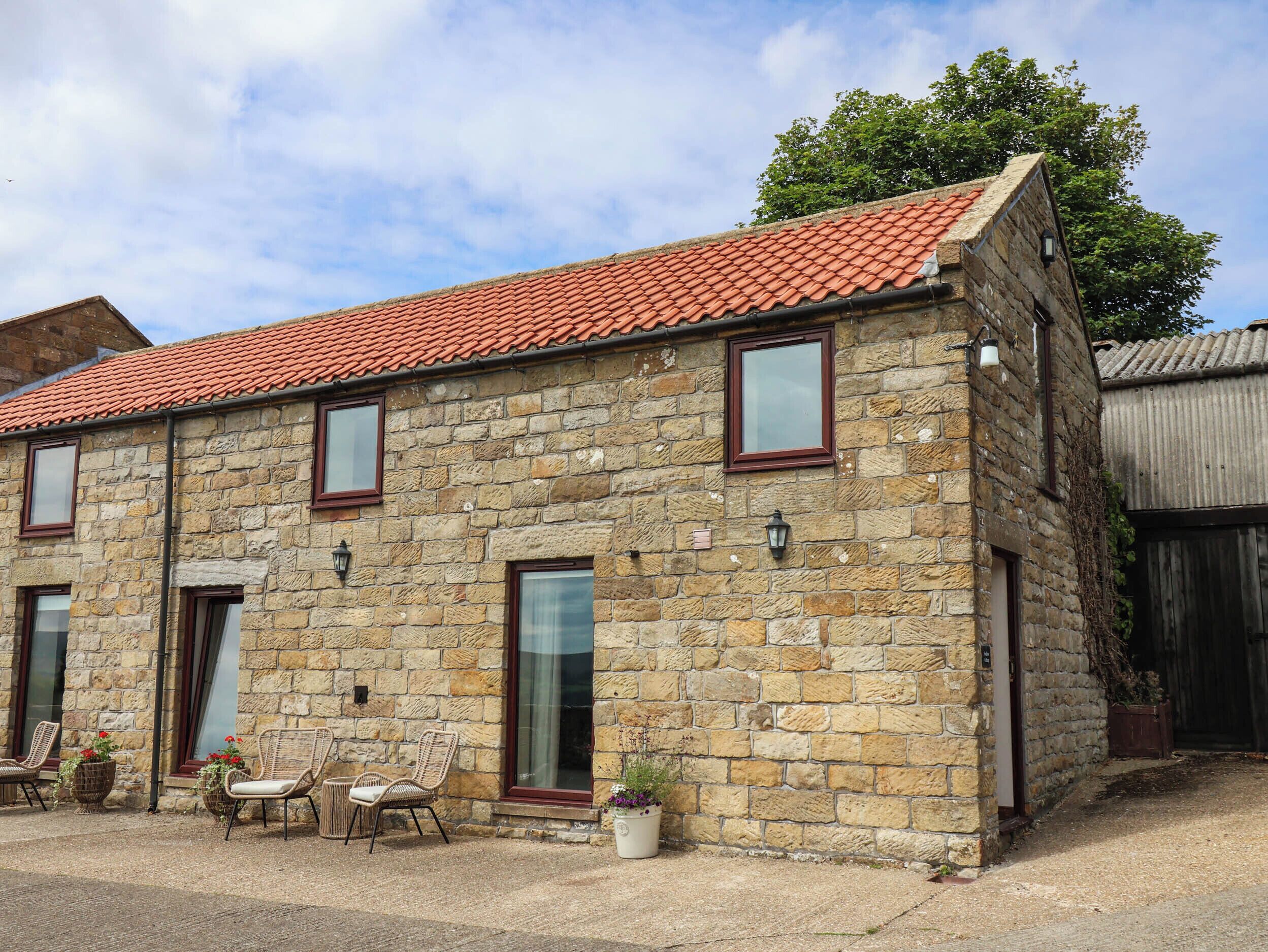 A stone building with a red-tiled roof, multiple windows, and outdoor seating.