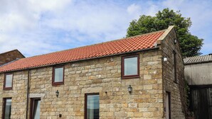 A stone building with a red-tiled roof, multiple windows, and outdoor seating. - Swallow Cottage (Whitby)