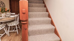 A staircase with a wooden handrail and carpeted steps leading to a dining area with a table set for two. - Swallow Cottage (Whitby)