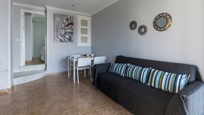 Uma sala de estar com um sofá cinza escuro, uma mesa de jantar com cadeiras e uma escada que leva a outro cômodo.