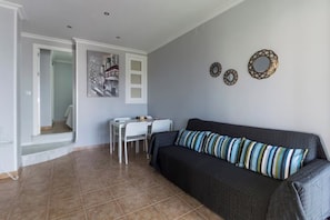 A living room with a dark grey sofa, a dining table with chairs, and a staircase leading to another room. - Apartment with Ocean Views in Fuentebravía Beach (EL PUERTO DE SANTA MARIA)