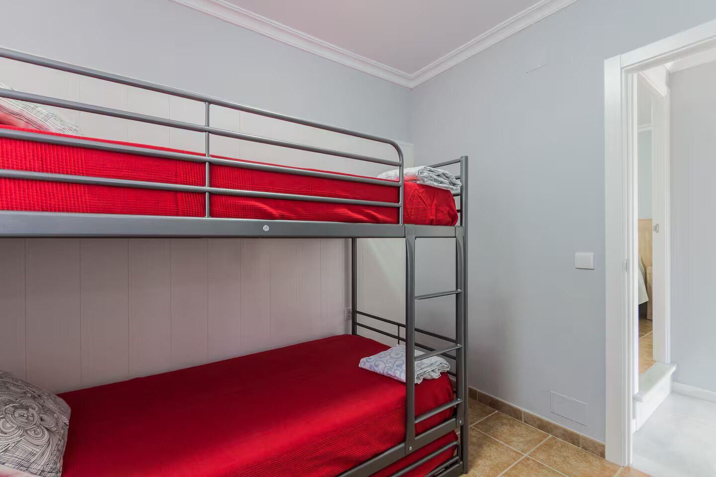 Ein Etagenbett mit roter Bettwäsche in einem Zimmer mit weißen Wänden und einer Tür.