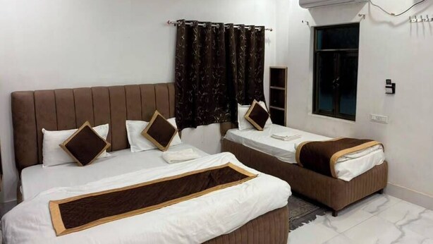 Ein Hotelzimmer mit einem großen Bett, zwei kleineren Betten, einem Deckenventilator, einer Klimaanlage und einem Fenster mit Vorhängen.