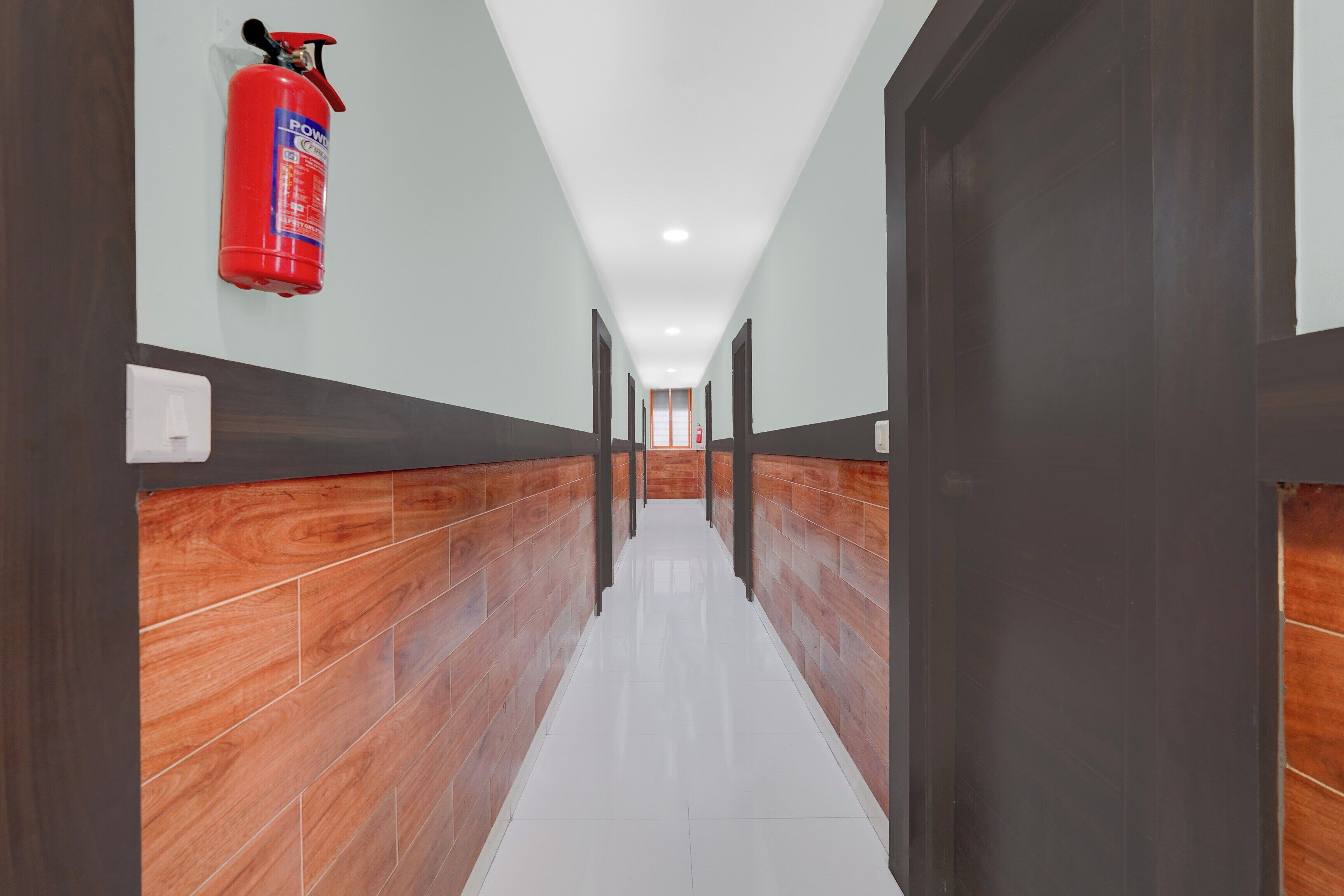 Un pasillo con un extintor montado en la pared, paneles de madera en las paredes y suelo de baldosas.