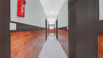 A hallway with a fire extinguisher mounted on the wall, wooden paneling on the walls, and a tiled floor.