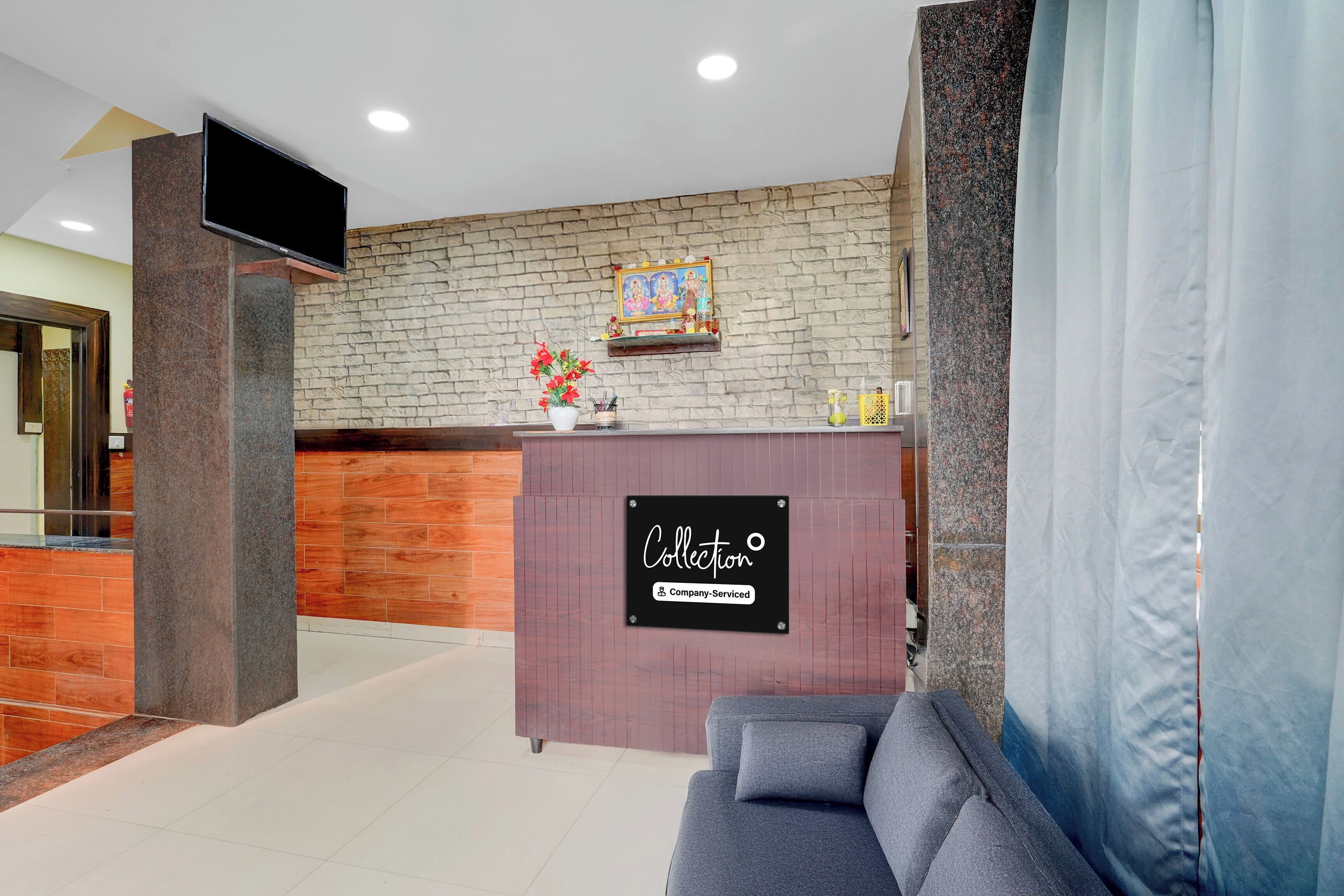 Zona de recepción con pared de ladrillo, mostrador de madera, sofá gris y televisión montada.