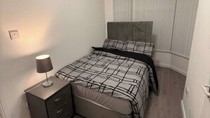 Un dormitorio con cama, mesita de noche, lámpara y ventana con persianas.