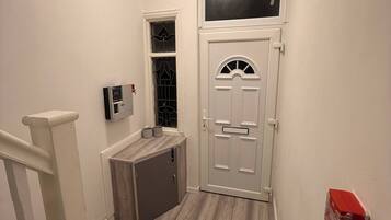 A hallway with a white door, a small window, and a wall-mounted thermostat.