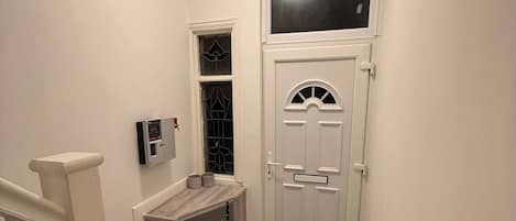 Un pasillo con una puerta blanca, un ventanal pequeño y un termostato instalado en la pared.