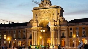 A large, historic archway with intricate carvings and a statue on top, surrounded by a plaza with a few people and a trash bin. - Praça do Comércio Romantic Apartment (Lisbon)