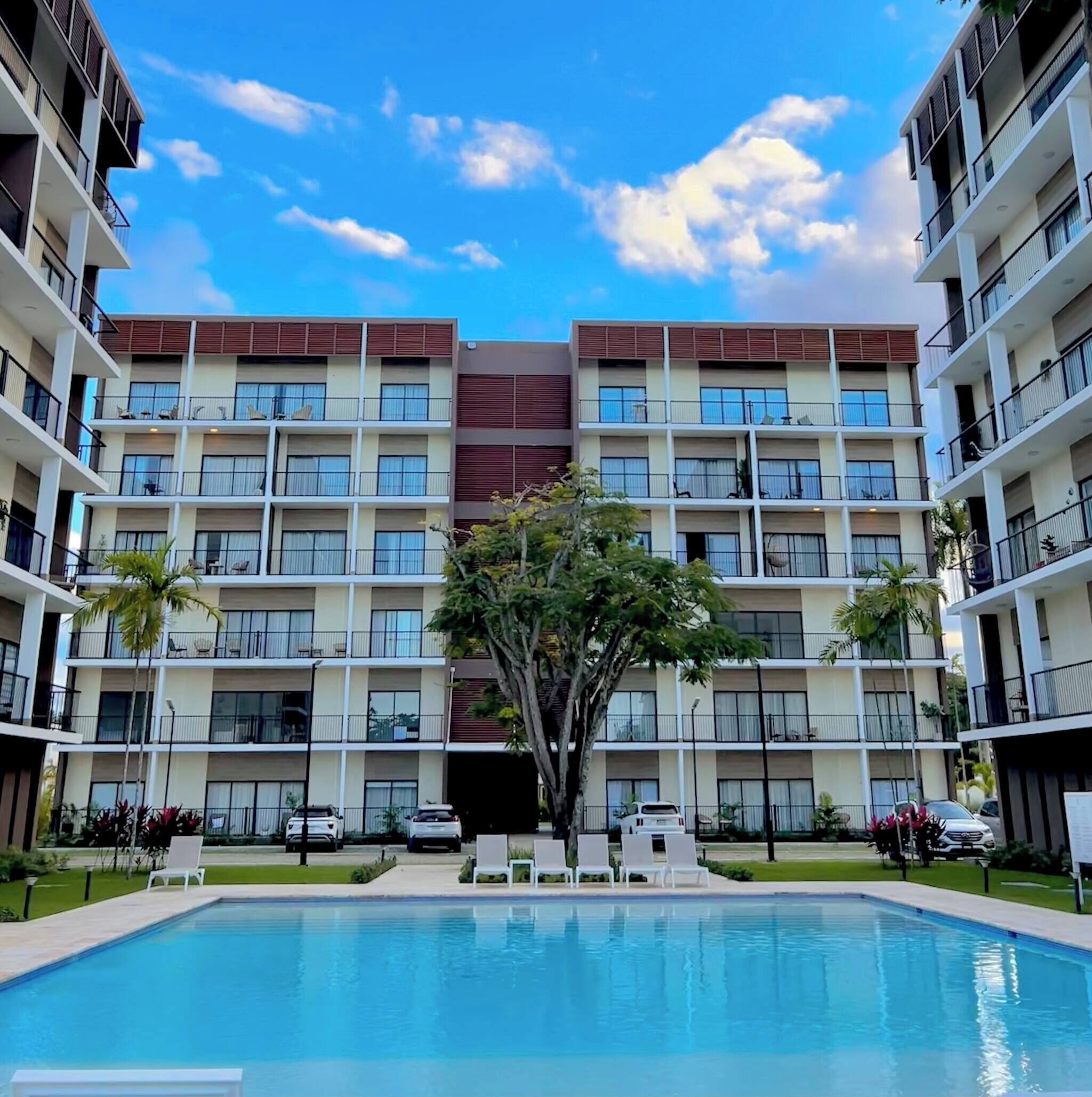 A multi-story hotel with a central pool, balconies, and a clear sky.