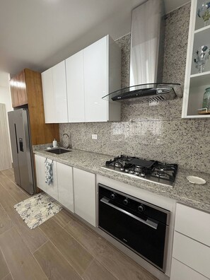 Una cocina moderna con armarios blancos, un refrigerador de acero inoxidable, una estufa a gas y un lavavajillas.