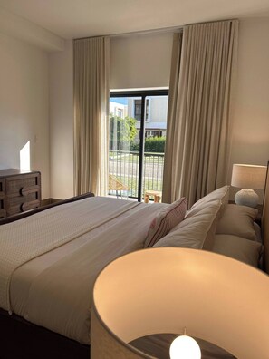 A hotel room with a large bed, a bedside table with a lamp, and a view of the outside. - Sorelipeaceful Retreat at Green One Playa Dorada (Puerto Plata)