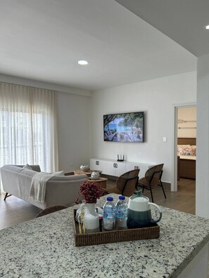 A modern living room with a sofa, a dining area, and a kitchen in the background. - Sorelipeaceful Retreat at Green One Playa Dorada (Puerto Plata)