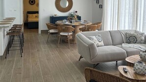 A modern living room with a sofa, dining table, and chairs. There is a kitchen area with a counter and stools. - Sorelipeaceful Retreat at Green One Playa Dorada (Puerto Plata)