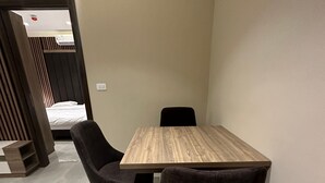 Quarto de hotel com uma mesa de madeira, duas cadeiras pretas, uma cama com cabeceira e um chão de azulejos.