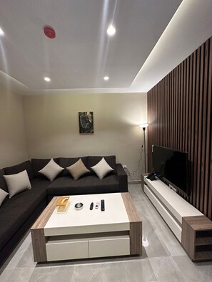 Un salon moderne comprenant un canapé d’angle, une table basse, un téléviseur à écran plat et un système audio fixé au mur.