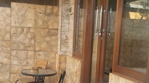 Een terras met een ronde tafel en stoelen, een stenen muur en een glazen deur met een metalen handgreep.