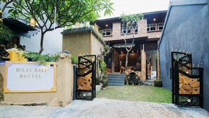 Een hostel ingang met een bord waarop 'BULAN BALI HOSTEL' staat, een hek en een trap naar het gebouw.