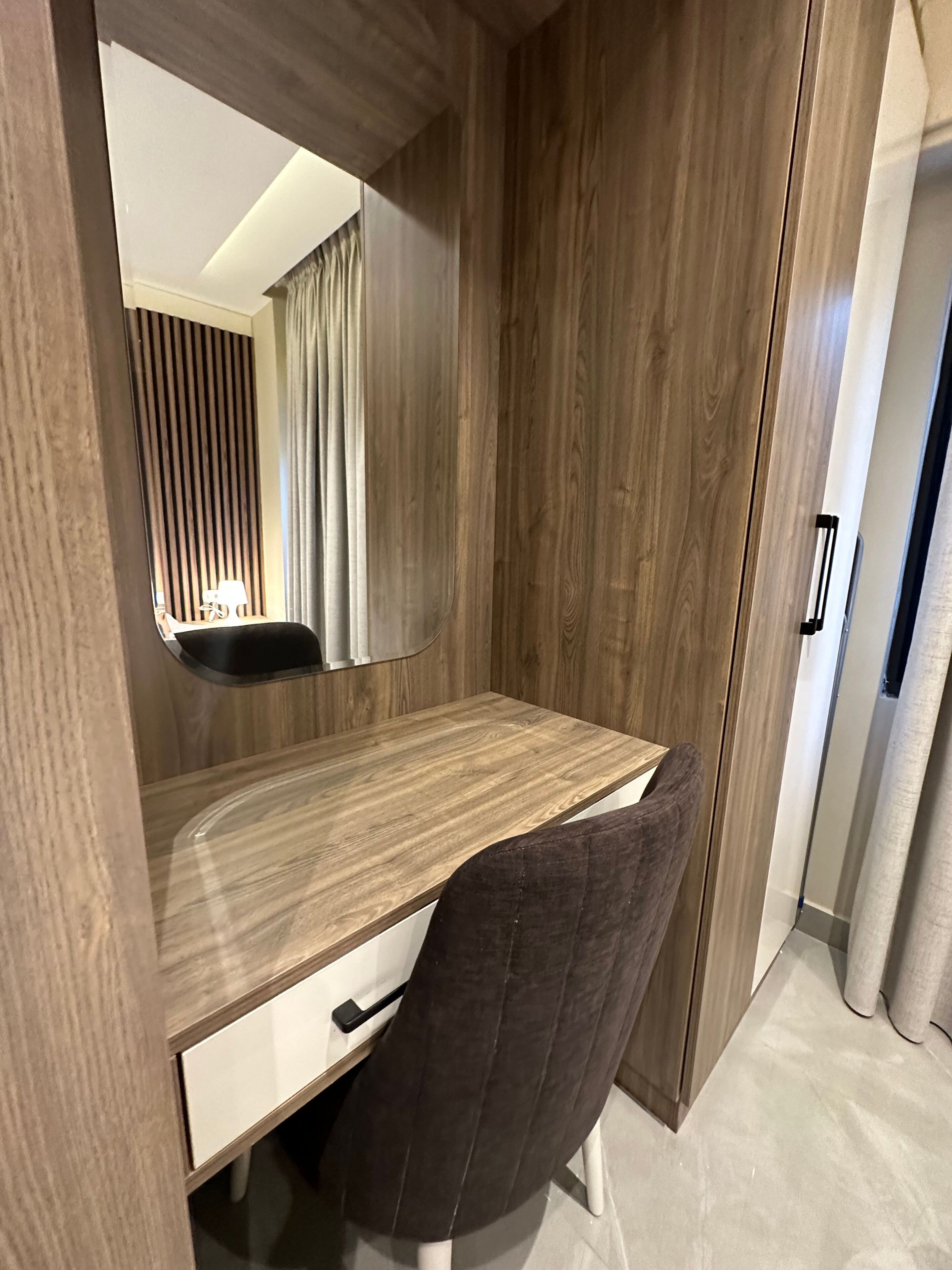 Ein modernes Zimmer mit Schreibtisch aus Holz, einem Stuhl, einem Spiegel und einer Tür.