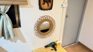 A room with a wooden floor, a small wooden table with a hairdryer, a woven mirror, and a wall-mounted artwork. - Room-tranquil Retreat in the Heart of Ba (Bangkok)