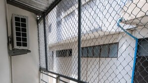 A balcony with a round table and two wicker chairs, a chain-link fence, and a building in the background. - Room-tranquil Retreat in the Heart of Ba (Bangkok)