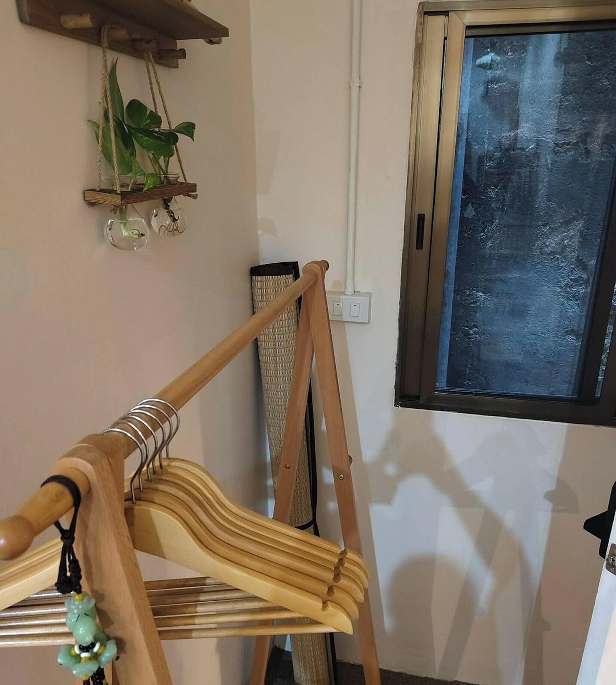 Una habitación con una silla de madera, una ventana, un estante con plantas y un enchufe en la pared.
