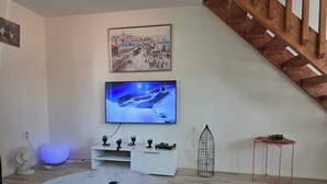 Un soggiorno moderno con una TV a schermo piatto montata sulla parete, un tavolino da caffè in marmo, un piccolo tavolo consolle bianco con oggetti decorativi, un tappeto nero e morbido e una scala in legno.