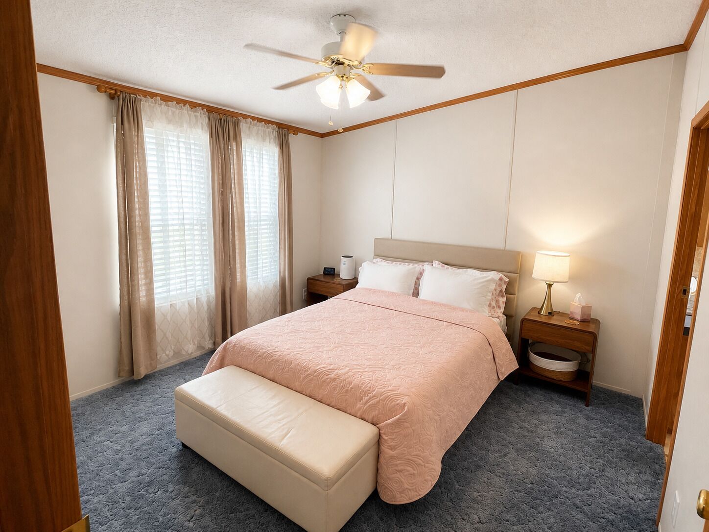 A bedroom with a bed, a bench, a ceiling fan, a nightstand, and a lamp.