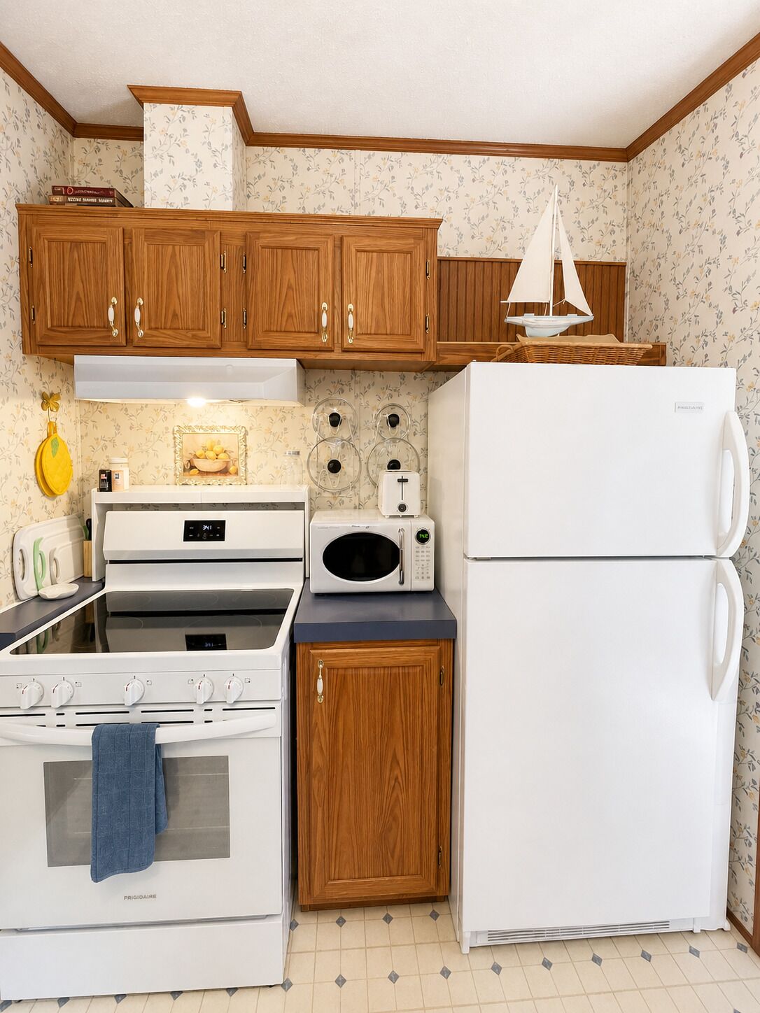 A compact kitchen with wooden cabinets, a stove, a microwave, and a refrigerator.