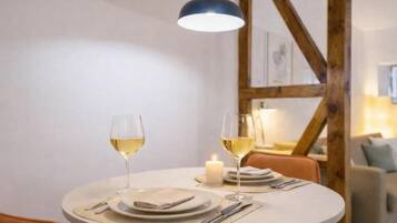 Una mesa redonda para comer con dos copas de vino blanco, una vela y un mantel individual.
