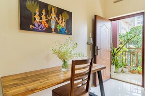 Una habitación con un banco de madera, un jarrón con flores, una puerta que da a un espacio exterior con plantas y un cuadro en la pared.