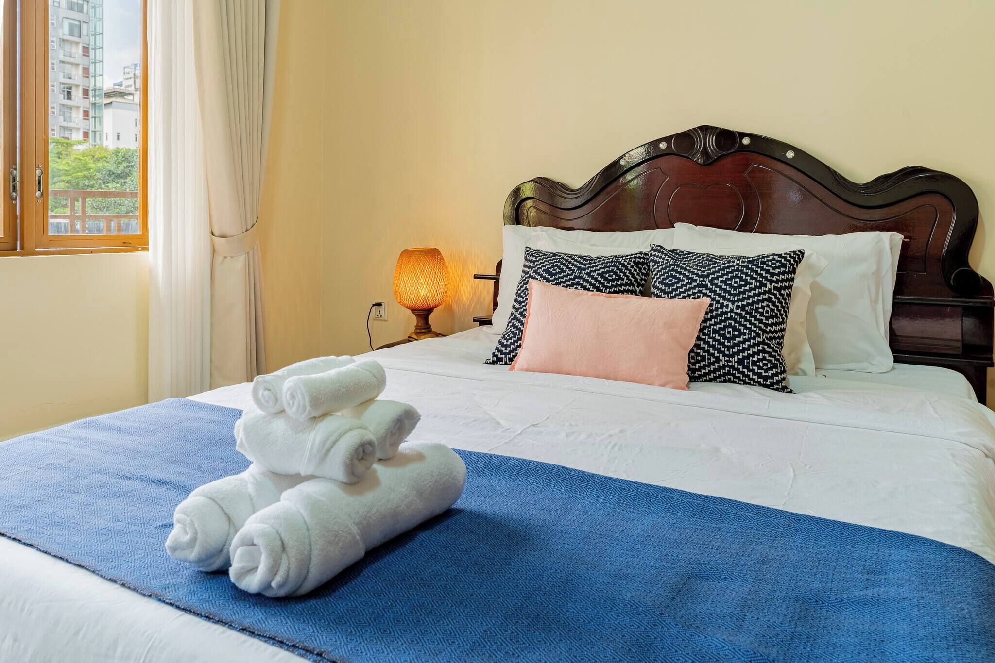 A hotel room with a neatly made bed, a blue blanket, and a stack of white towels.