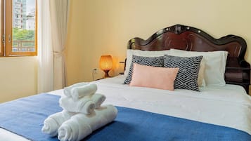 A hotel room with a neatly made bed, a blue blanket, and a stack of white towels.