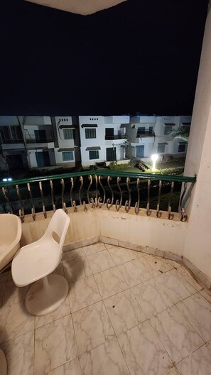 A corner of a room with a toilet, a chair, and a balcony railing.