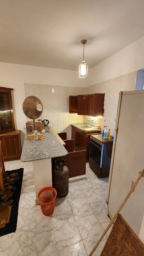 Una cocina compacta con encimera de granito, armarios de madera, estufa a gas y refrigerador.