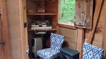 Une pièce de taille modeste, avec un intérieur en bois, une petite table, deux chaises à motifs, un radiateur et une fenêtre donnant sur un paysage verdoyant.
