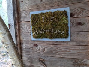 A wooden wall with a moss-covered sign that reads 'THE TREEHOUSE.'