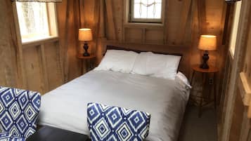 Une pièce en bois avec un lit, deux lampes, une fenêtre avec des rideaux et une chaise à motifs.