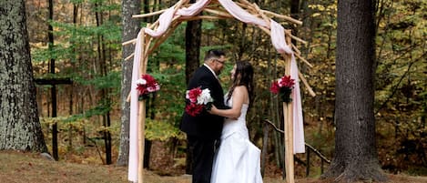 Una pareja bajo un arco de madera decorado con flores en un entorno boscoso.