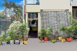 Un acceso de edificio con una escalera que lleva a una puerta, rodeado de plantas en macetas.