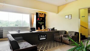 Zona de recepción con mostrador, sofá, sillón, ventilador de techo y ventana con vistas a árboles.