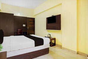 A hotel room with a bed, a television mounted on the wall, a small bedside table with a kettle, and a wooden wardrobe. - Collection O Summanahalli Bus Stand (Bangalore)