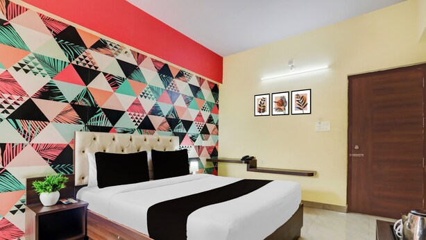 Una habitación de hotel con una cama, una mesita de noche, una planta, una pared con diseños geométricos y una puerta.