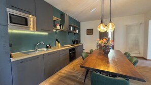 A modern kitchen with a built-in microwave, a sink, and a wooden dining table with chairs. - La Casa del Re, just 400 meters from Lake Idro (Anfo)