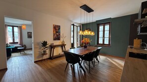 A dining area with a wooden table, black chairs, and a chandelier. There is a painting on the wall and a window with curtains. - La Casa del Re, just 400 meters from Lake Idro (Anfo)
