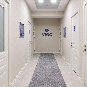 A hallway with a tiled floor, white walls, and doors on both sides. There is a logo with the word 'VIGO' on the wall.