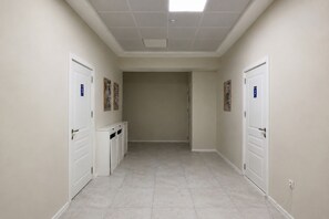 Un pasillo con puertas blancas, cada una identificada con un número. El piso está cubierto de baldosas y las paredes tienen un tono neutro.