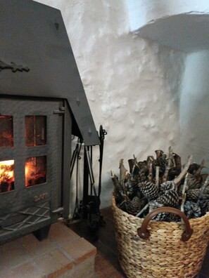 A fireplace with logs, a woven basket with branches, and a stone wall.