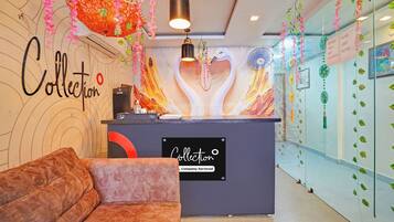 Un espace d’accueil d’hôtel au design moderne, comprenant un canapé, un comptoir de réception et des œuvres d’art décoratives murales.